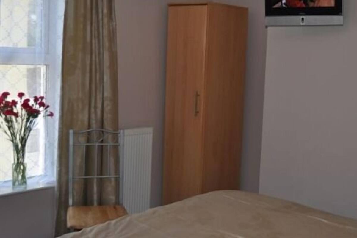 A bedroom with a bed, a wooden wardrobe, a radiator, and a window with curtains.