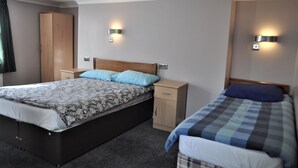 A bedroom with a large bed, a smaller bed, a wardrobe, and two wall-mounted lights. - Grand Hastings (St Leonards-On-Sea)