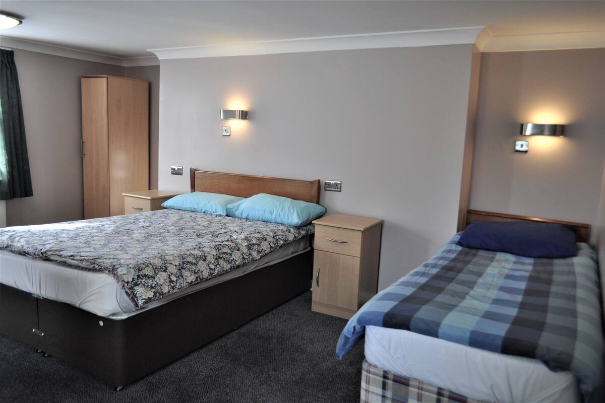 A bedroom with a large bed, a smaller bed, a wardrobe, and two wall-mounted lights.