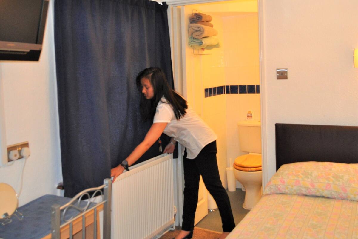 A hotel room with a bed, a radiator, a television mounted on the wall, and a bathroom visible through an open door.