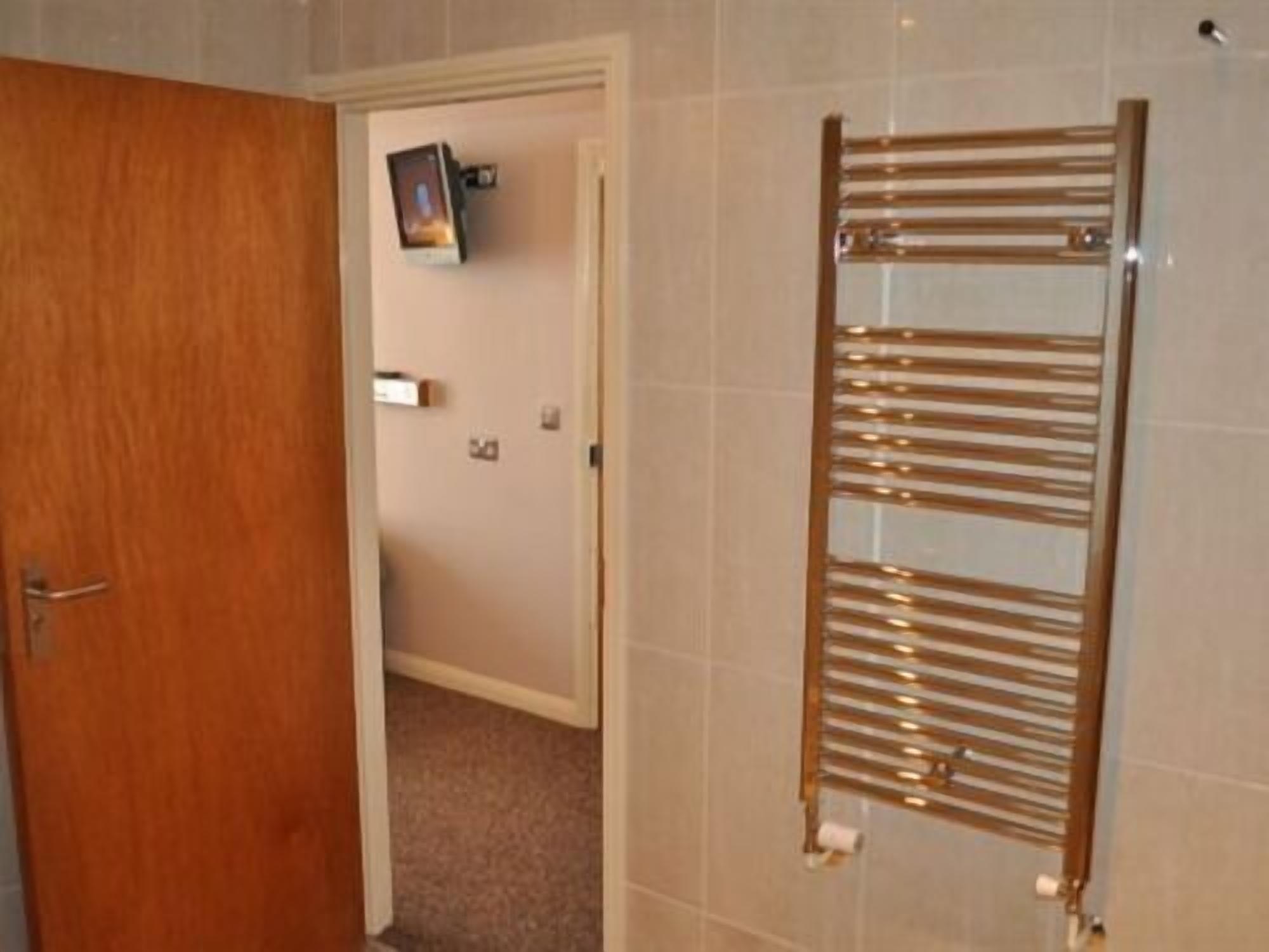 A bathroom with a wooden towel rack, a door, and a wall-mounted light fixture.