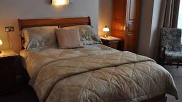 Habitación de hotel con una cama grande, dos mesitas de noche con lámparas, un armario de madera y un sillón estampado.