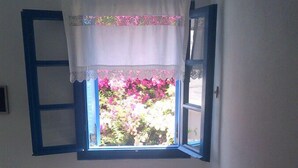 Una habitación con ventana, persianas azules, una cortina blanca y vistas a flores rosas.