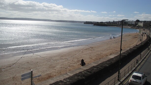 A beach with a clear sky, a sandy shore, and a stone wall running parallel to the beach. - Grosvenor House (Torquay)