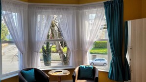 A room with a bay window, two chairs, a small table, and a view of the street outside. - Grosvenor House (Torquay)