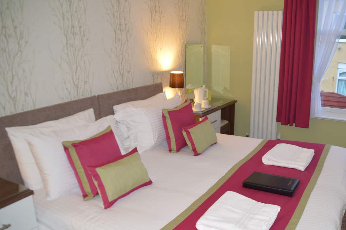 A hotel room with a neatly made bed, a bedside table with a lamp, a mirror, and a window with curtains.