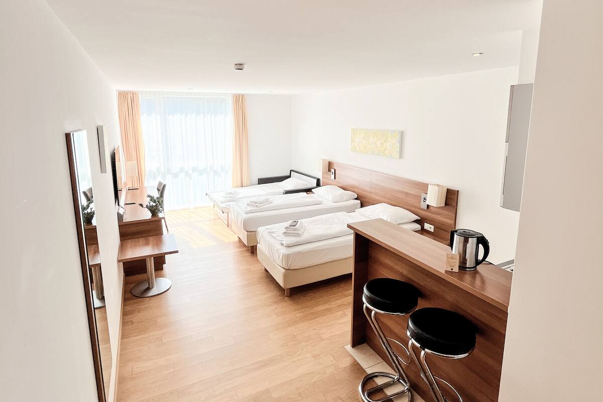 Een hotelkamer met een houten vloer, een bed, een bureau, twee barkrukken en een koffieapparaat.