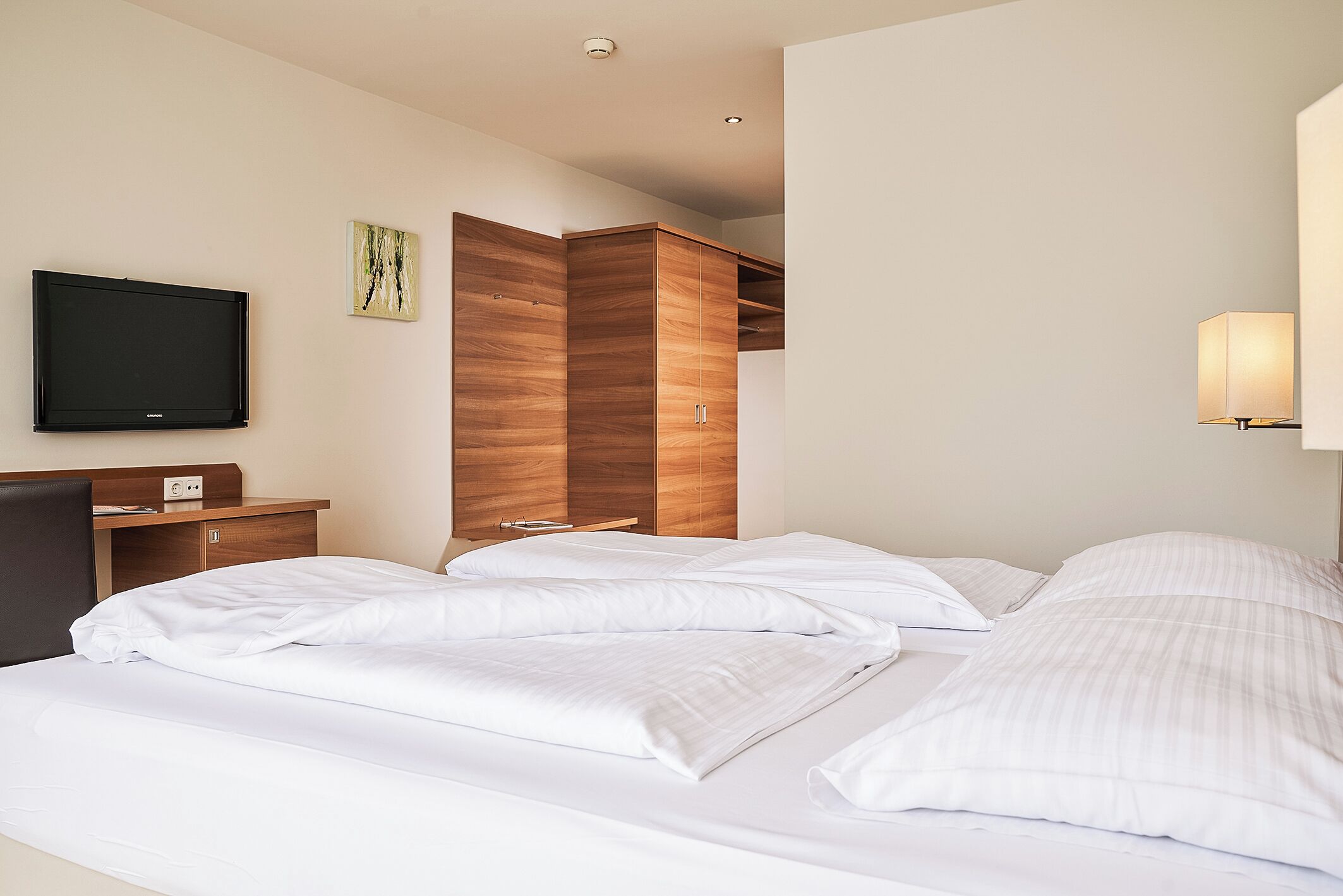 Una habitación de hotel con una cama, un televisor de pantalla plana, un armario de madera y una lámpara de noche.