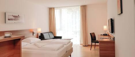 Habitación de hotel con cama, escritorio, silla, televisor y ventana con cortinas.