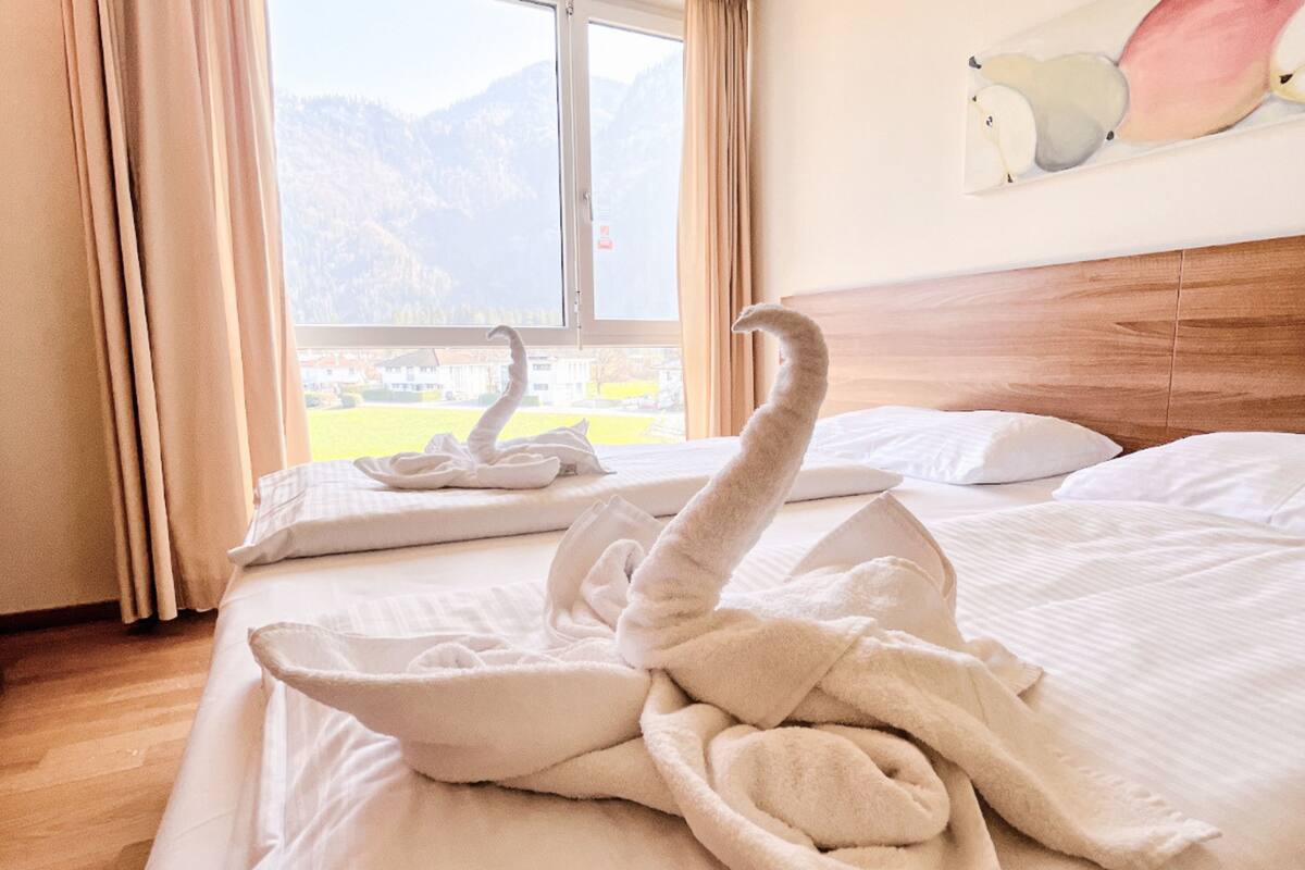 Een hotelkamer met een bed, een raam met gordijnen en uitzicht op bergen.