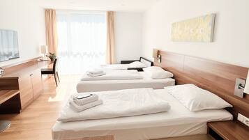 Habitación de hotel con tres camas, un escritorio, televisor y ventana con cortinas.