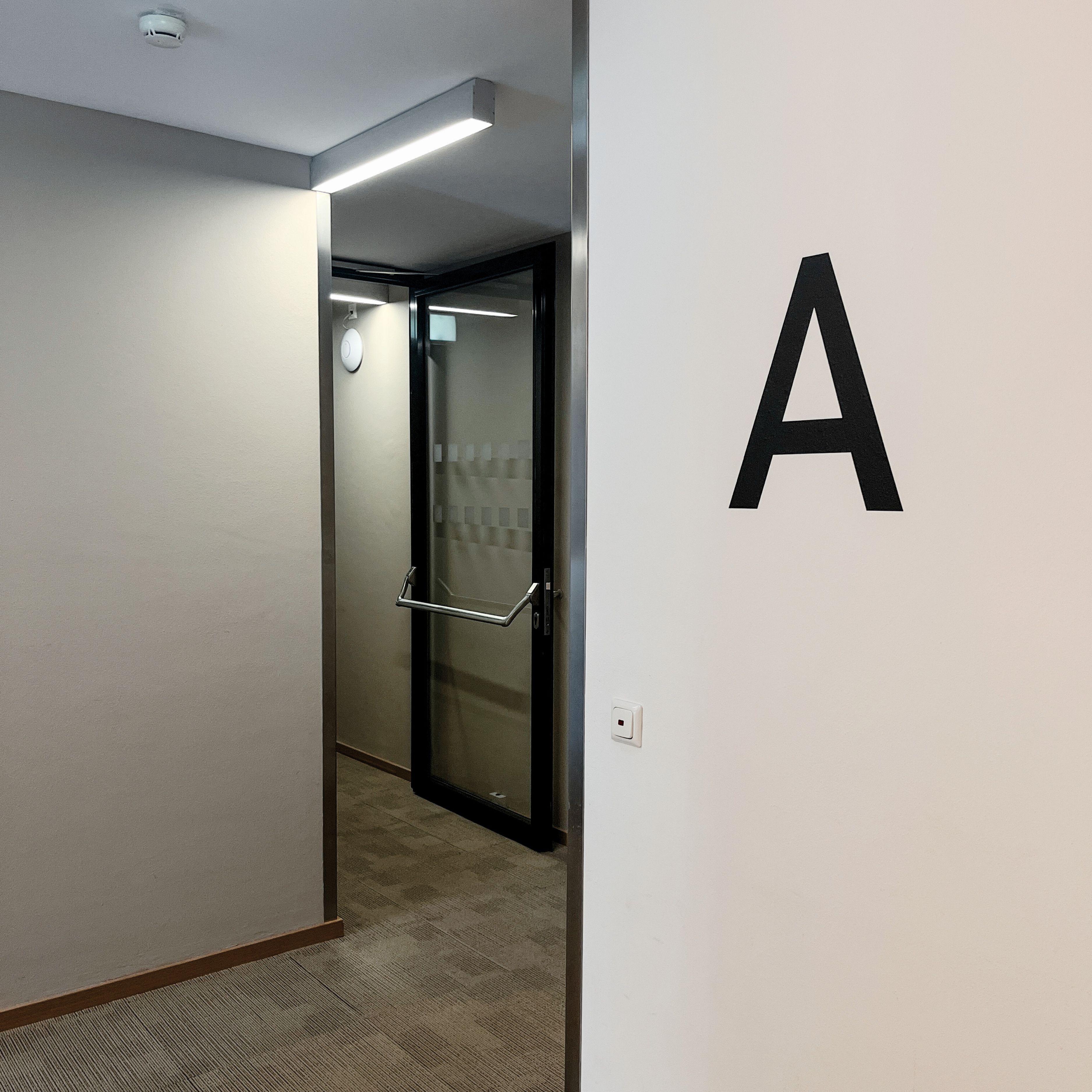 A hallway with a door marked 'A' leading to a room with a glass door and a security camera.
