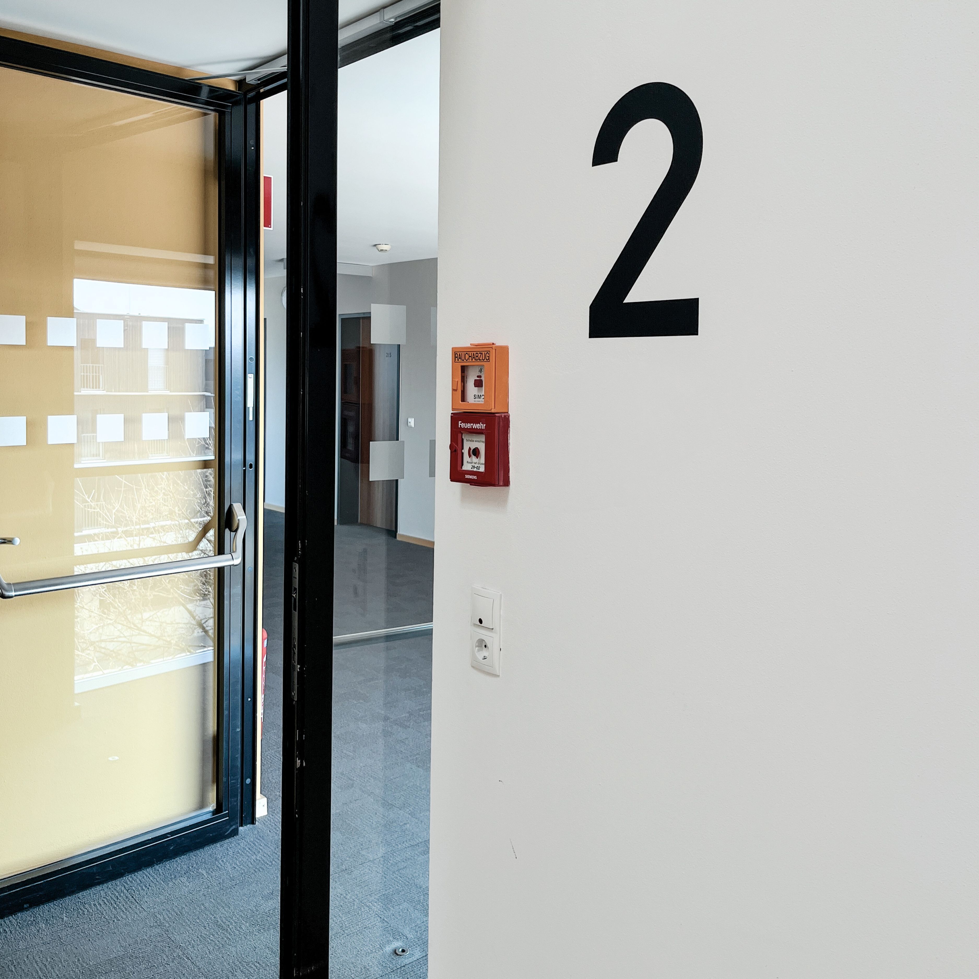 A hallway with a door leading to a room, a wall with the number 2, and a fire safety box.