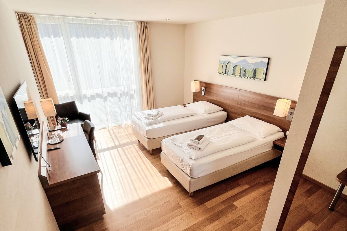 Een hotelkamer met twee bedden, een bureau, een stoel, een lamp en een schilderij aan de muur.