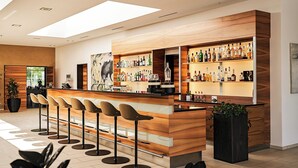 Un espace bar moderne avec un comptoir en bois, de nombreux tabourets et une variété de bouteilles d’alcool.