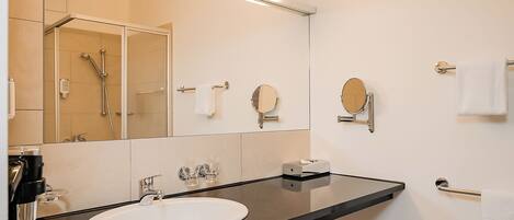 A modern bathroom with a white sink, a large mirror, and a glass-enclosed shower.