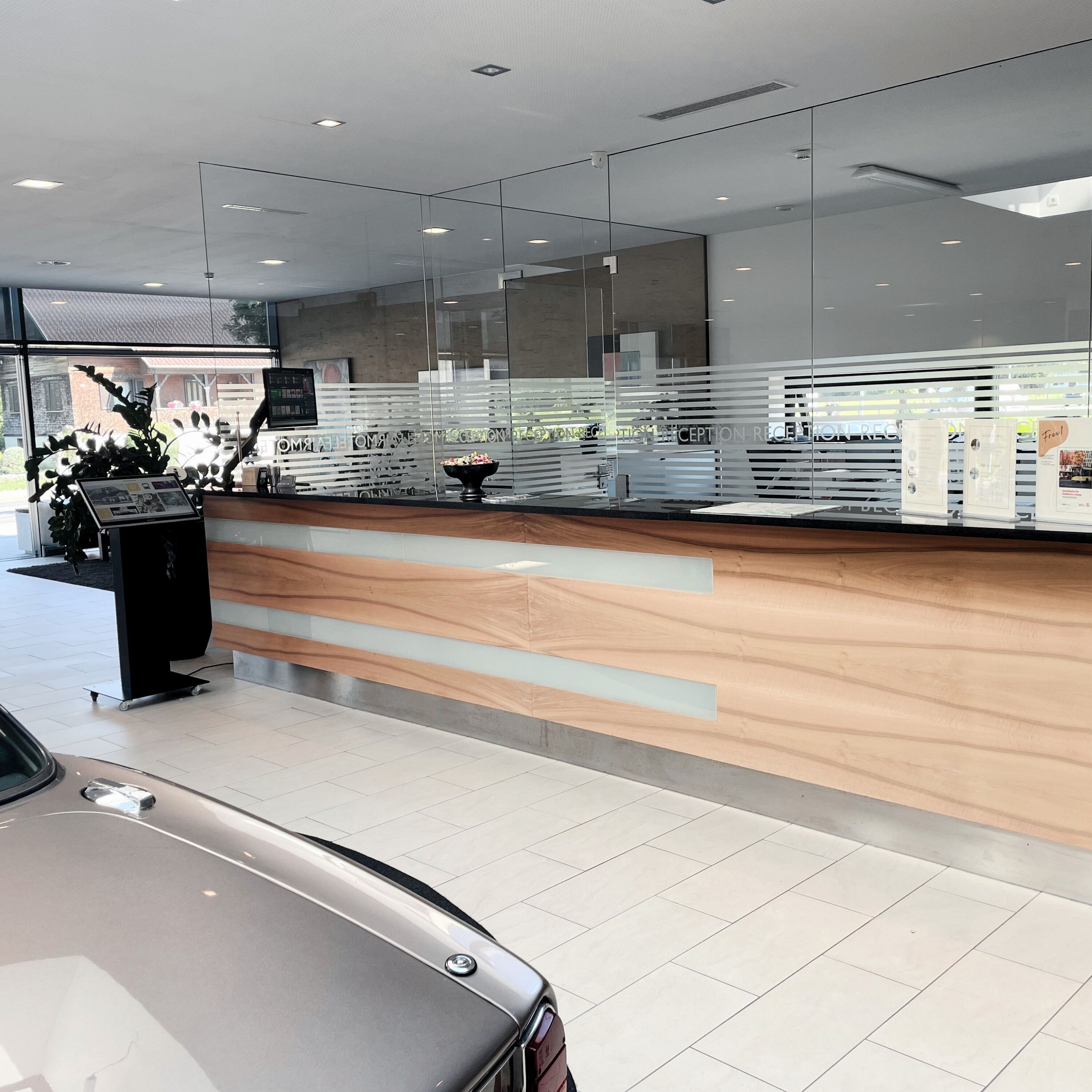 A modern reception area with a wooden counter, glass partitions, and a car parked in the foreground.