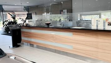 A modern reception area with a wooden counter, glass partitions, and a car parked in the foreground.
