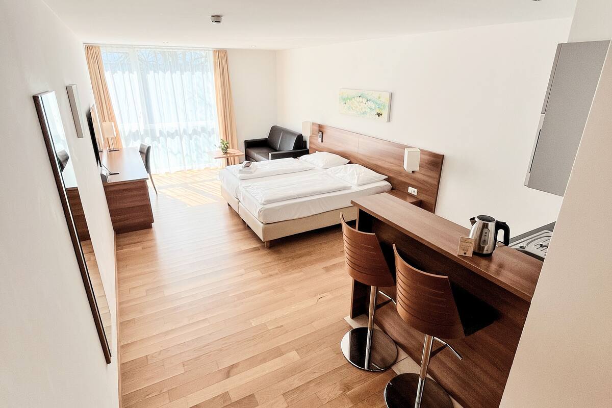 Een moderne hotelkamer met een bed, een bureau, twee stoelen, een koffiezetapparaat en een schilderij aan de muur.