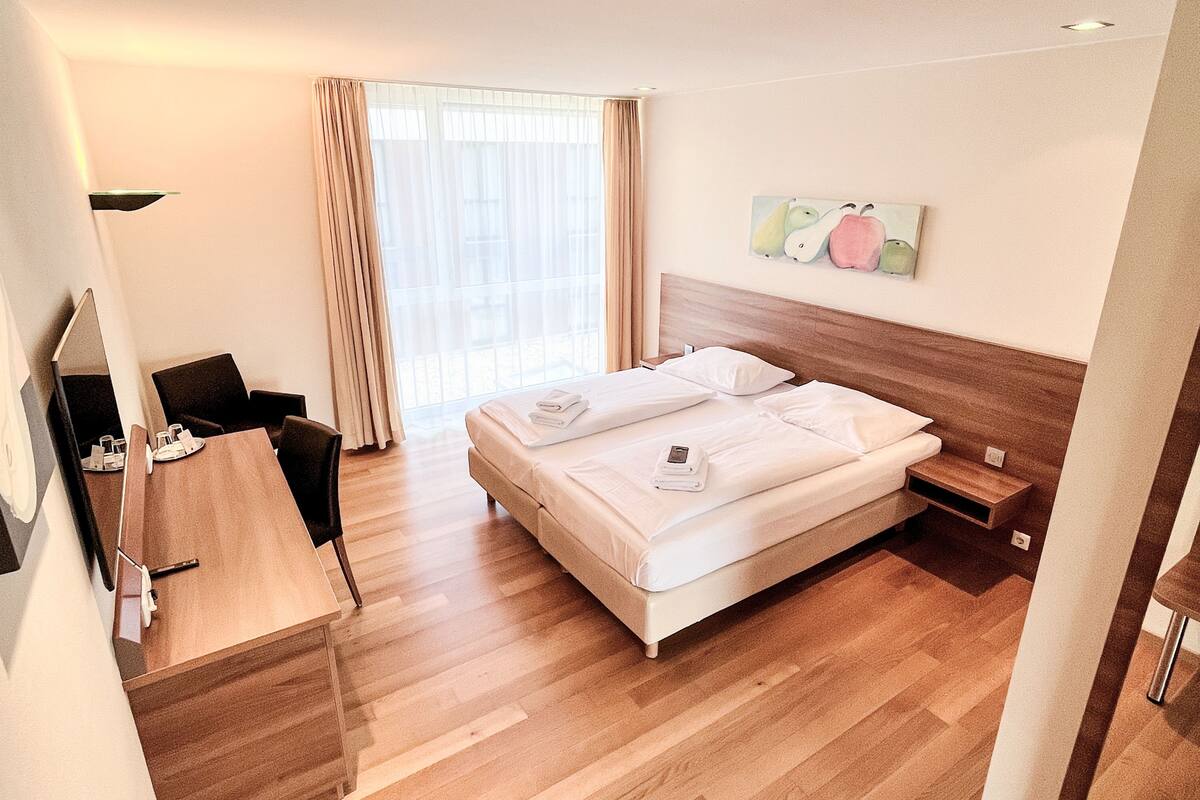 Een hotelkamer met een bed, nachtkastje, stoel, bureau en een schilderij aan de muur.