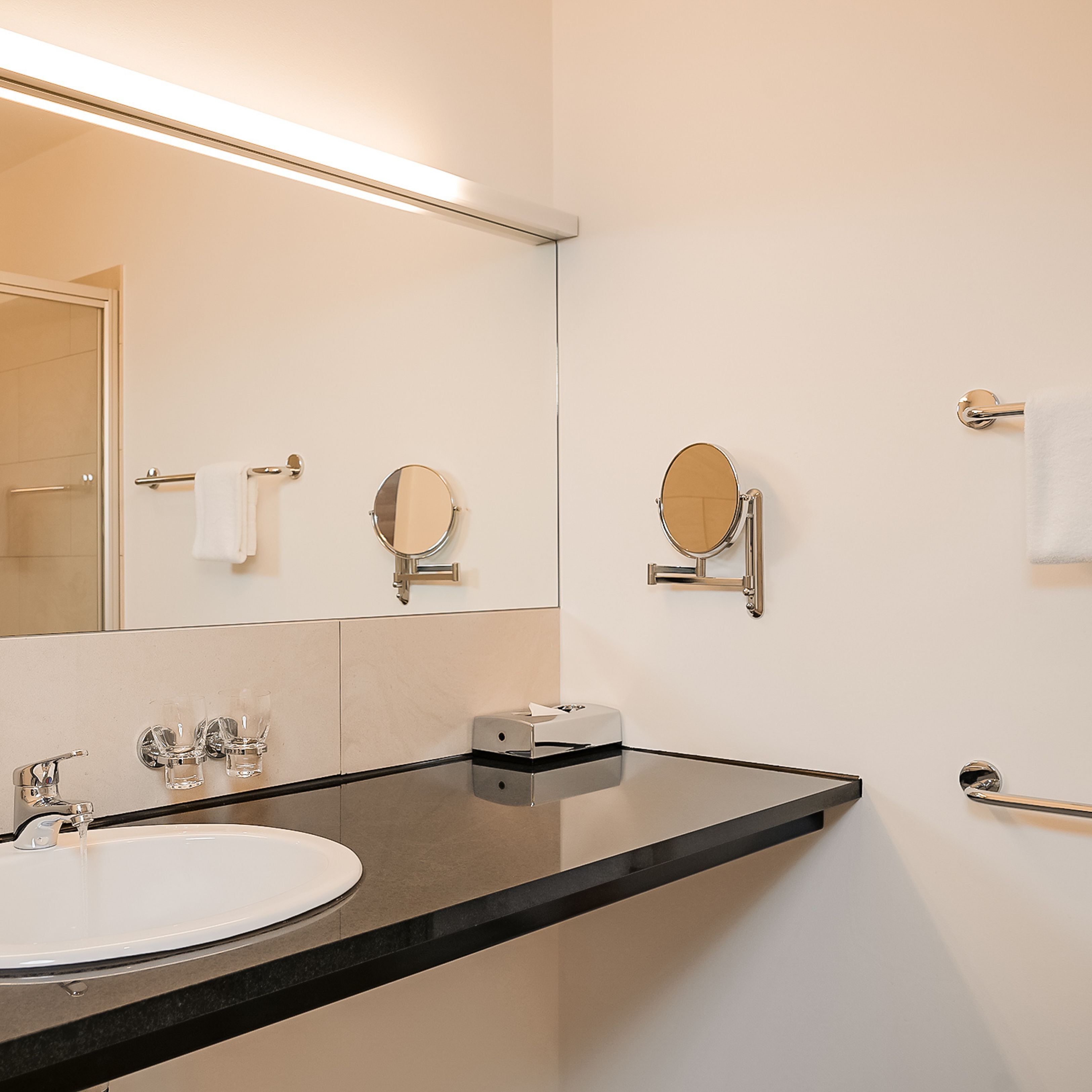 Une salle de bain moderne avec un grand miroir, un lavabo et deux miroirs fixés au mur.