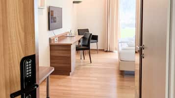 Une chambre d’hôtel avec un bureau en bois, un téléviseur fixé au mur, une chaise noire, un canapé blanc et une porte dotée d’un système de verrouillage à clavier.