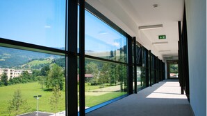 Un couloir doté de grandes fenêtres, offrant une vue sur un paysage verdoyant, et un panneau indiquant une sortie.