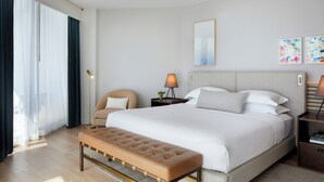 A hotel room with a large bed, a bench, a chair, a bedside table with a lamp, and a window with curtains. - Kimpton EPIC Hotel by IHG (Miami)