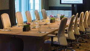Una sala de conferencias con una larga mesa, sillas y una pantalla que muestra la marca del hotel.