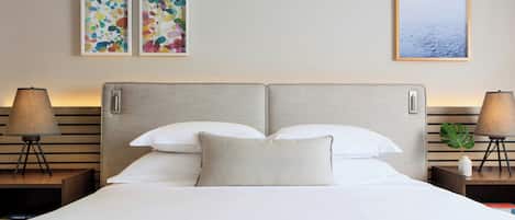 A hotel room with a bed, two nightstands, a lamp, a plant, and two abstract paintings on the wall.