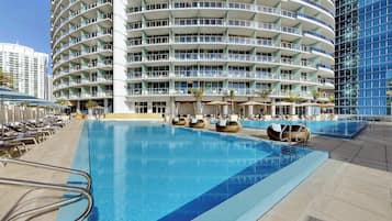 Un hotel con una amplia piscina exterior, varios balcones y sillones de sol.