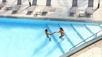 A swimming pool with lounge chairs and a tiled deck area.