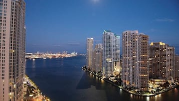 Une vue nocturne d’un paysage urbain au bord de l’eau, avec de hauts immeubles et un fleuve paisible.