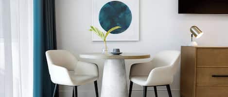 A modern dining area with a marble table, two chairs, a vase with a plant, and artwork on the wall.