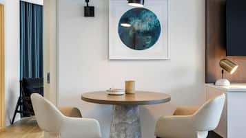 Een moderne kamer met een ronde marmeren tafel, twee stoelen, een lijst met een abstract schilderij en een bevestigde televisie.