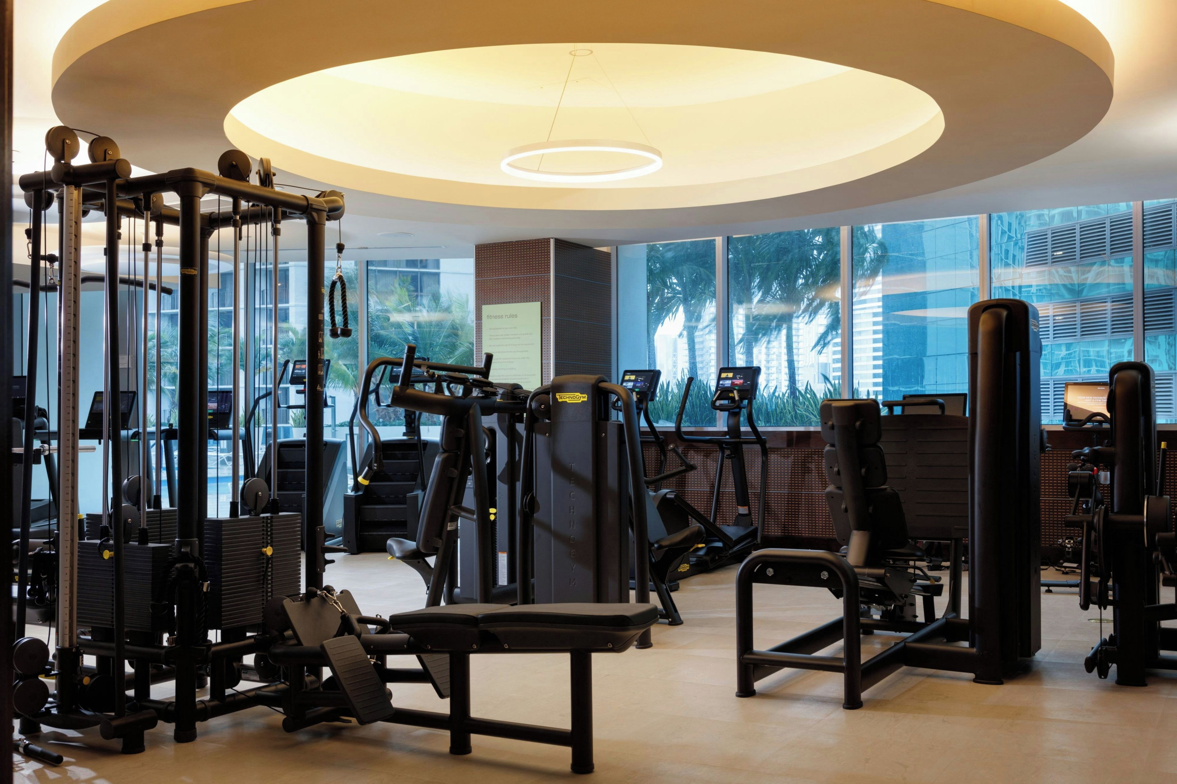 A gym with various exercise equipment, large windows, and a modern ceiling design.