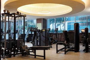 Une salle de sport équipée de divers appareils d’exercice, dotée de grandes fenêtres et d’un design moderne au niveau du plafond.