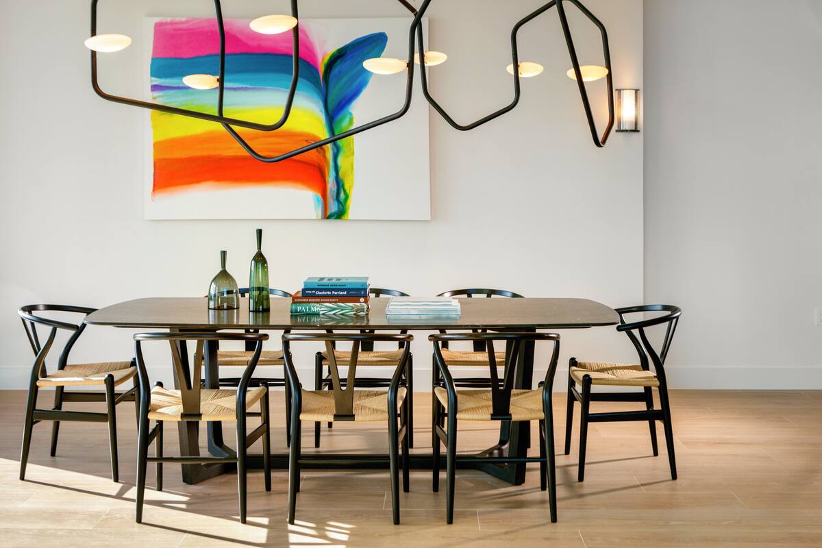 A dining area with a round table, six chairs, and a colorful abstract painting above.