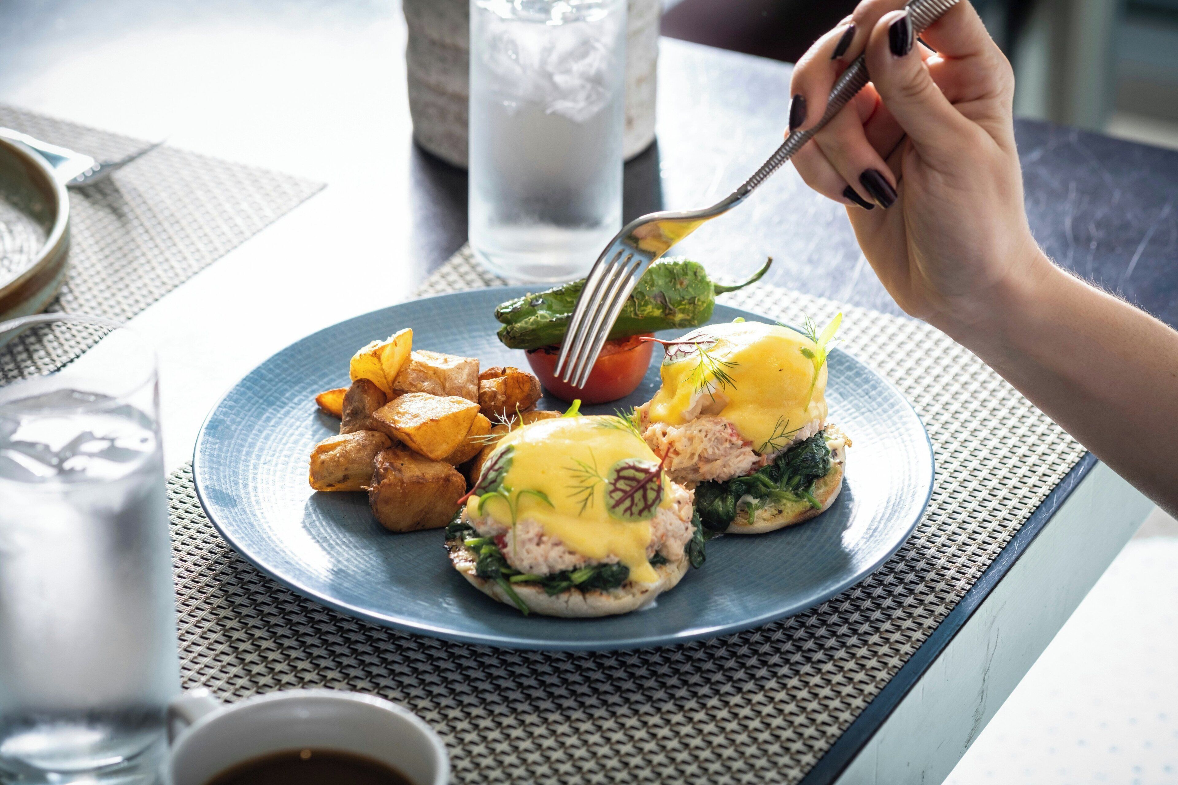 A plate of food with eggs benedict, roasted potatoes, and a small tomato.