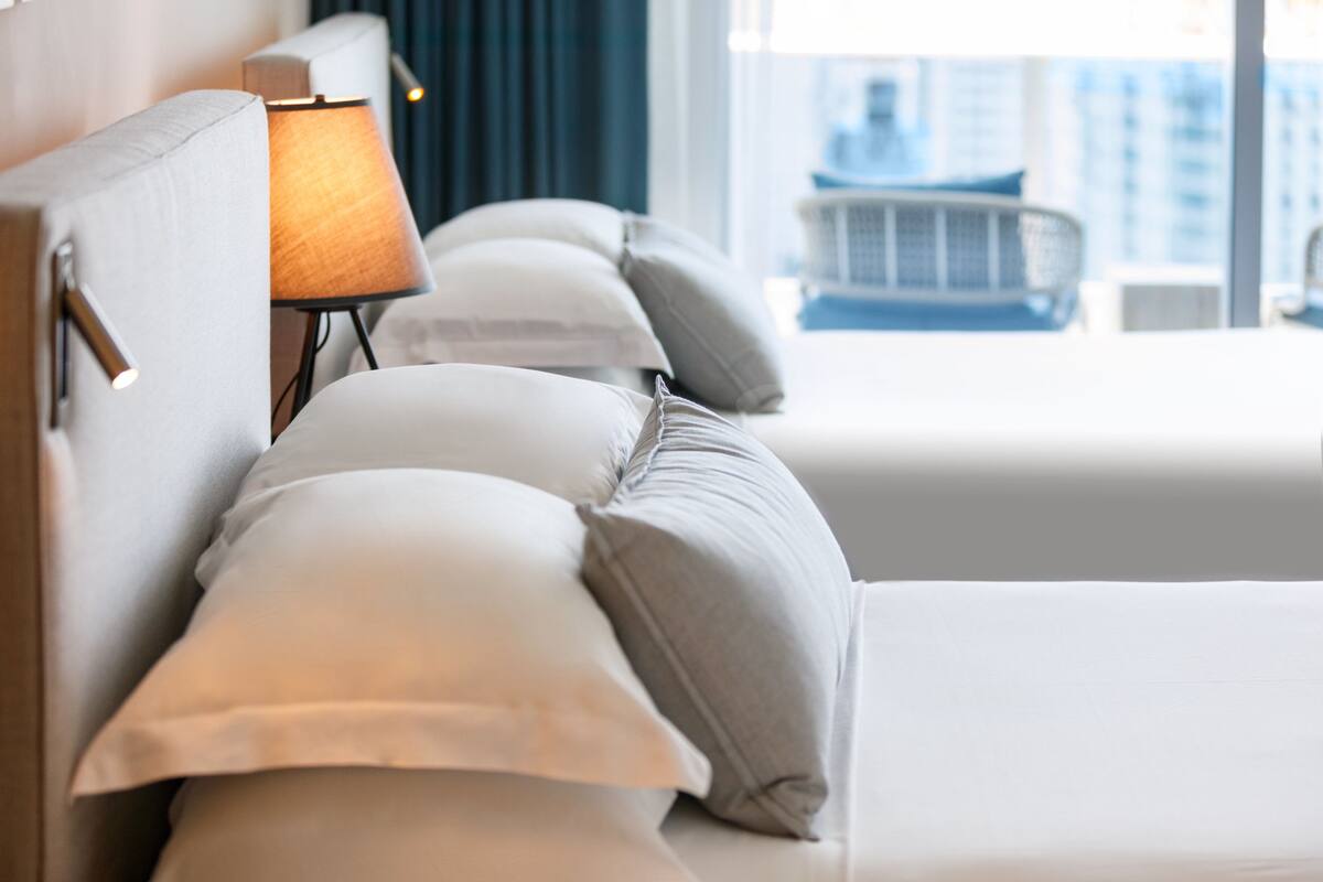 A hotel room with a bed, pillows, a lamp, and a view of buildings.