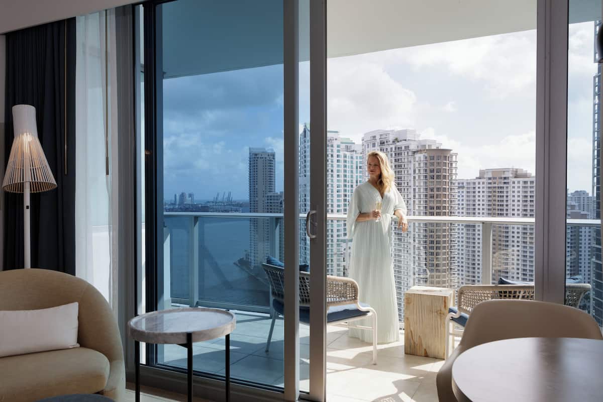 Une chambre d’hôtel moderne avec balcon, de grandes fenêtres et vue sur la ville.
