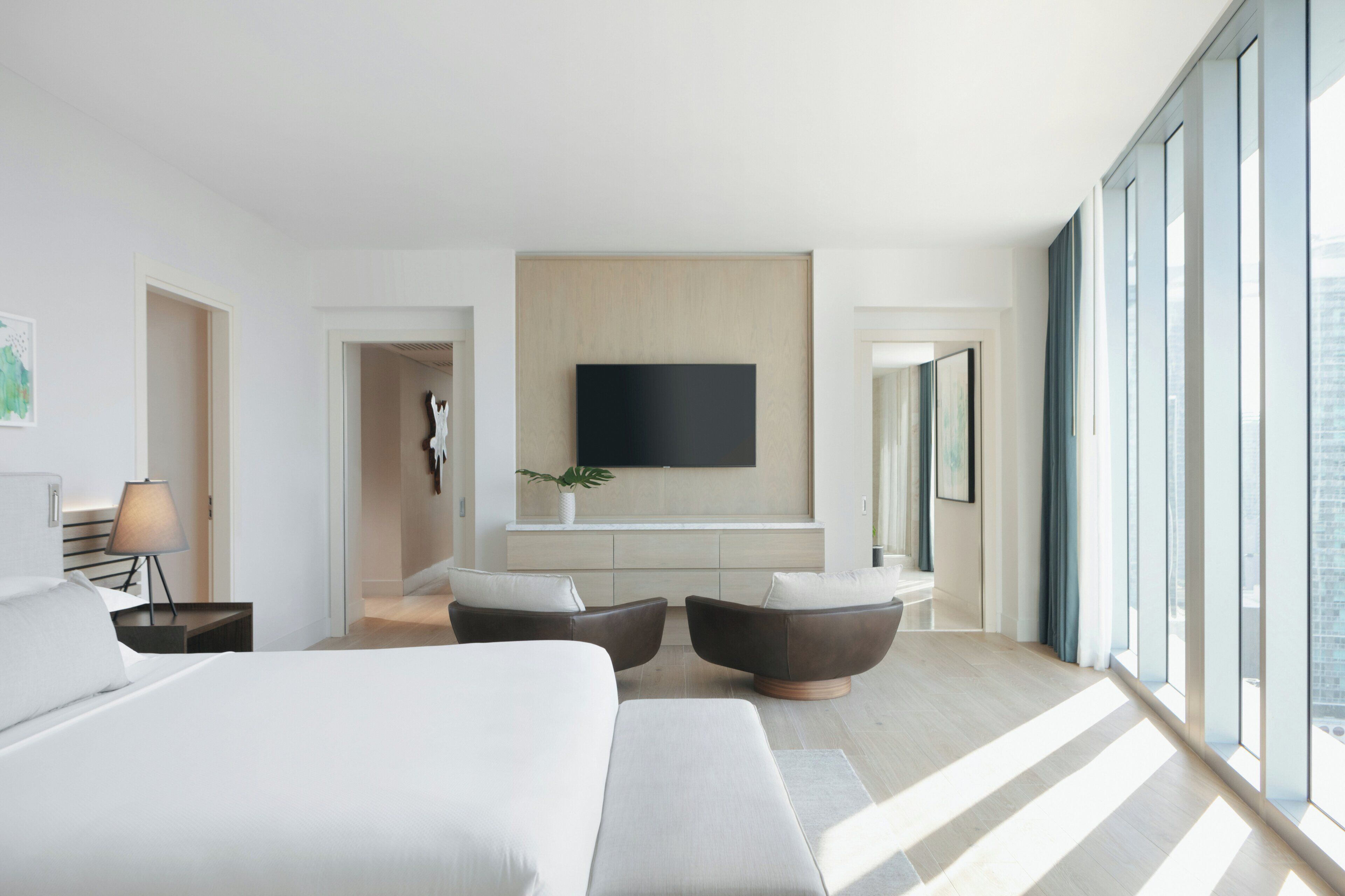 A modern hotel room with a large bed, a flat-screen TV mounted on the wall, and a seating area with two armchairs.