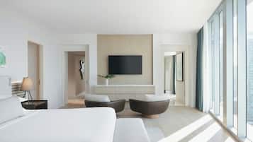 A modern hotel room with a large bed, a flat-screen TV mounted on the wall, and a seating area with two armchairs.