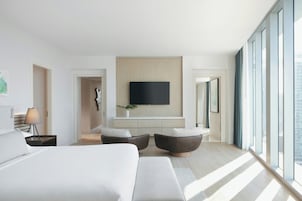 Une chambre d’hôtel moderne dotée d’un grand lit, d’un téléviseur à écran plat fixé au mur et d’un coin salon avec deux fauteuils.