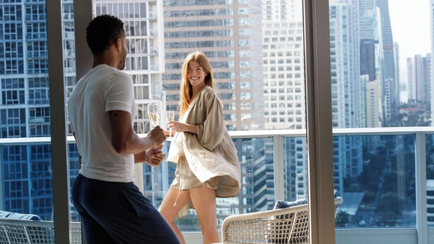 A man and a woman toasting with champagne glasses on a balcony with a cityscape view. - Kimpton EPIC Hotel by IHG (Miami)