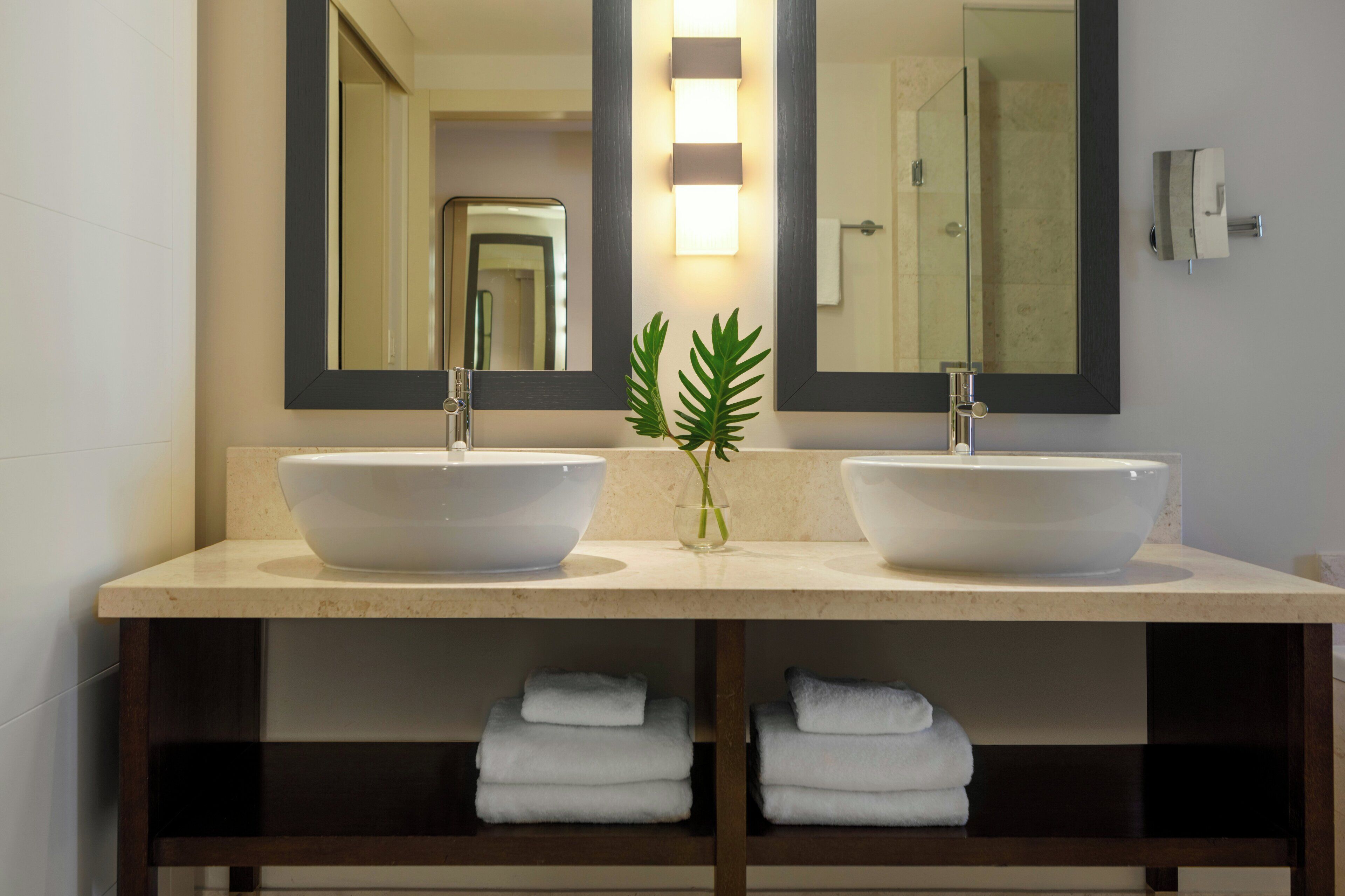 A bathroom with two white sinks, a large mirror, and a plant in a vase.