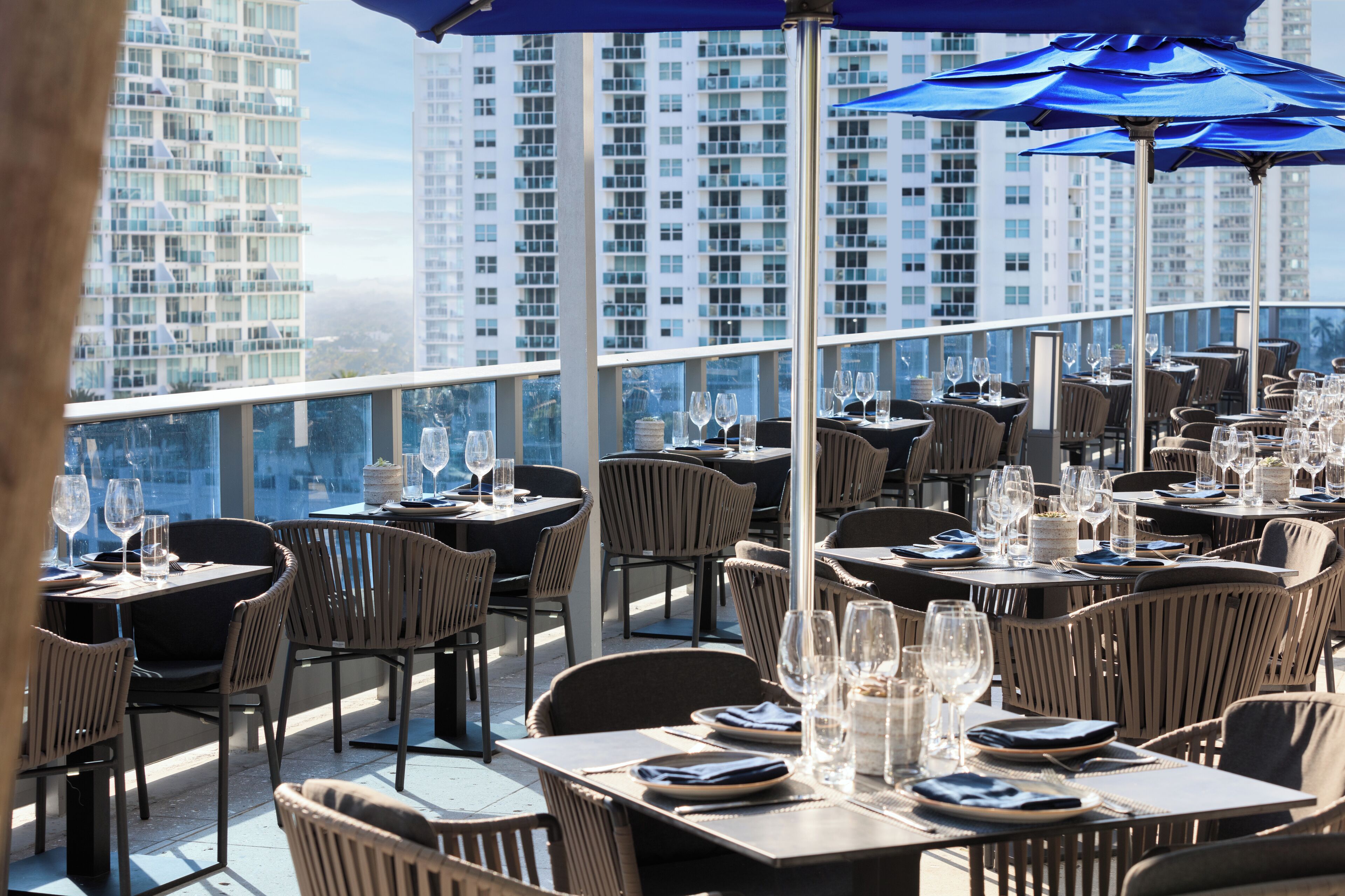 A rooftop restaurant with tables set for dining, overlooking a cityscape.