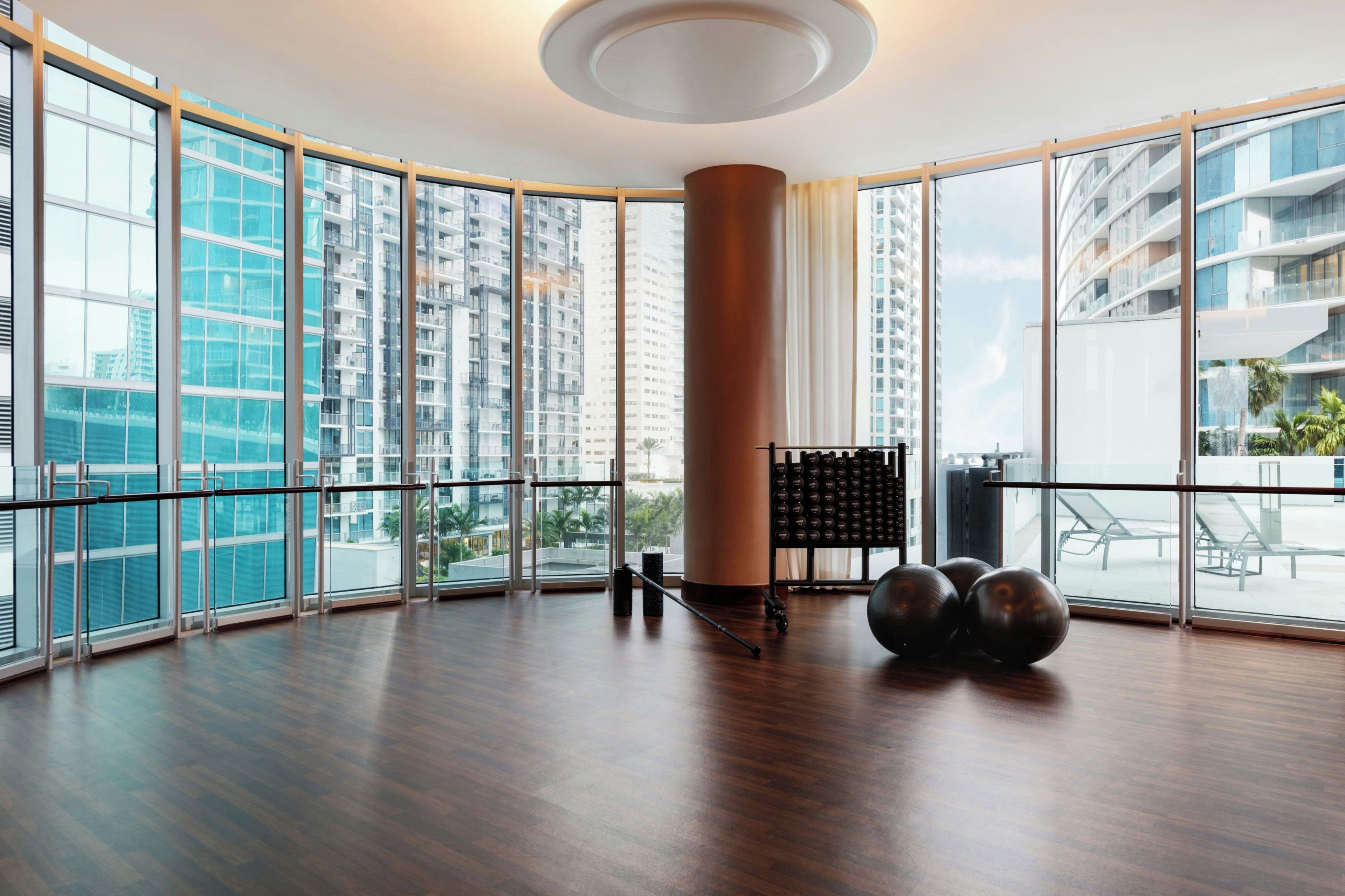 A spacious room with large windows, a wooden floor, and exercise equipment.