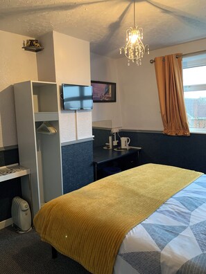 A hotel room with a bed, a desk, a television, and a window with curtains.