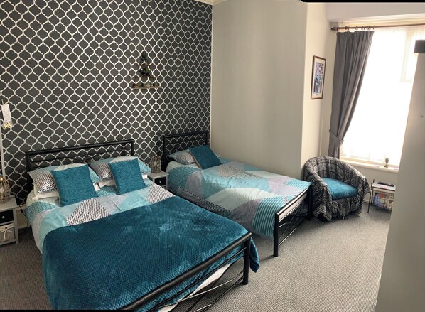 Una habitación con dos camas, una silla, una mesita de noche y una ventana con cortinas.